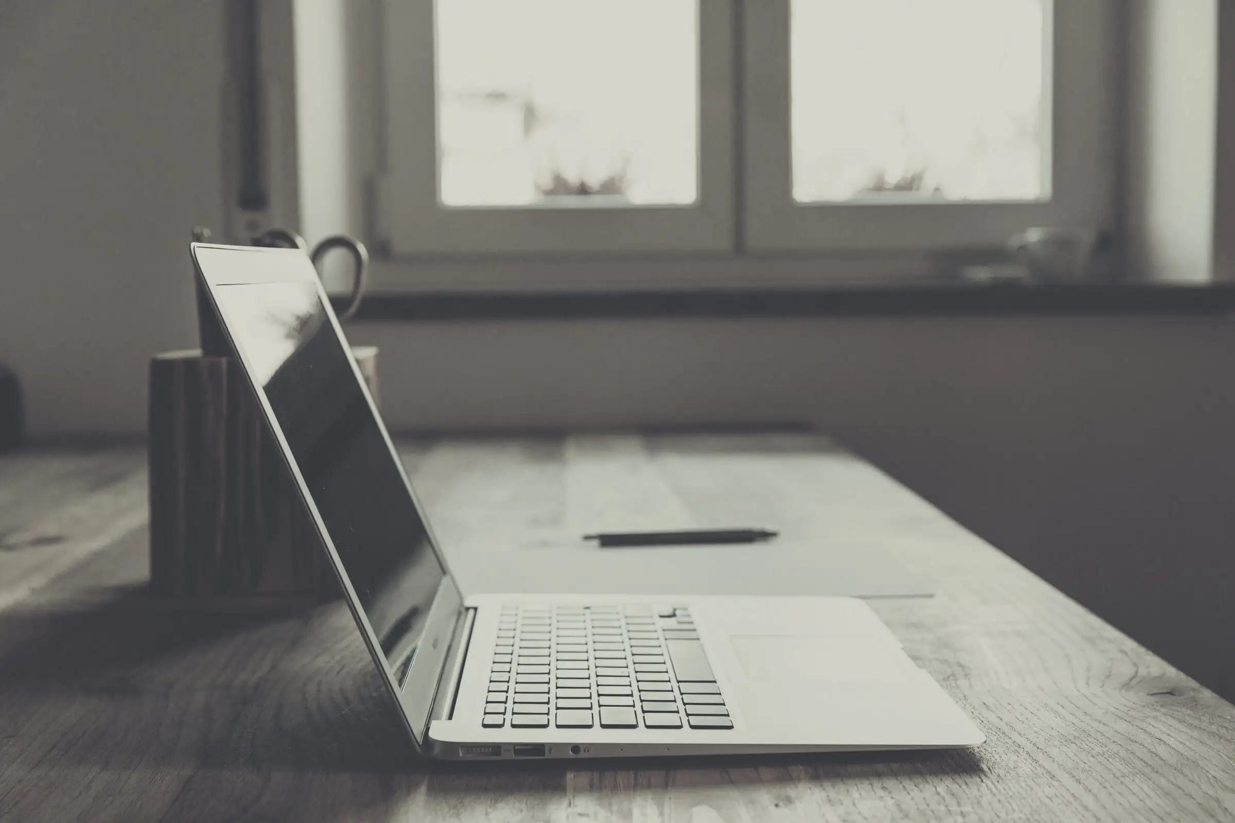 Nyitott laptop egy hosszú fa asztalon, a háttérben ablak